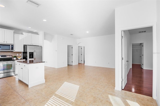 kitchen featuring dark stone countertops, backsplash, stainless steel appliances, white cabinets, and a kitchen island