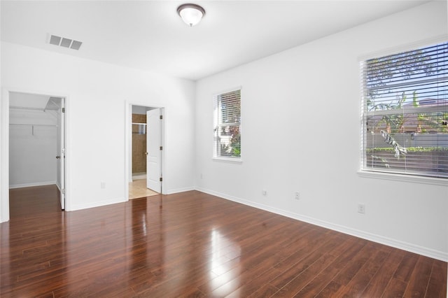 unfurnished bedroom featuring ensuite bath, dark hardwood / wood-style floors, a closet, and a spacious closet