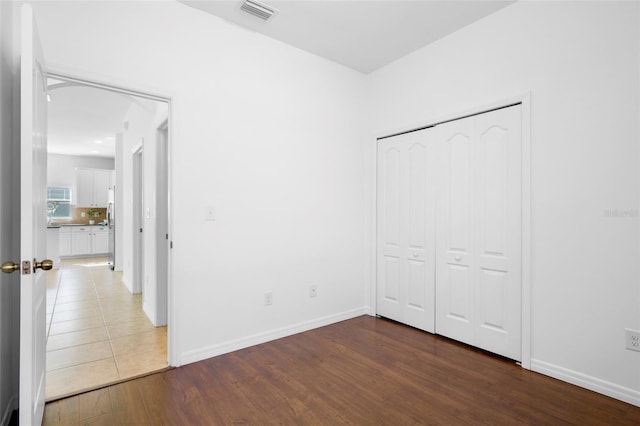 unfurnished bedroom with a closet, stainless steel fridge, and dark hardwood / wood-style floors