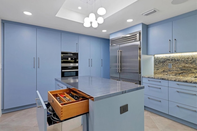 kitchen featuring a kitchen island, hanging light fixtures, a tray ceiling, stainless steel appliances, and blue cabinetry