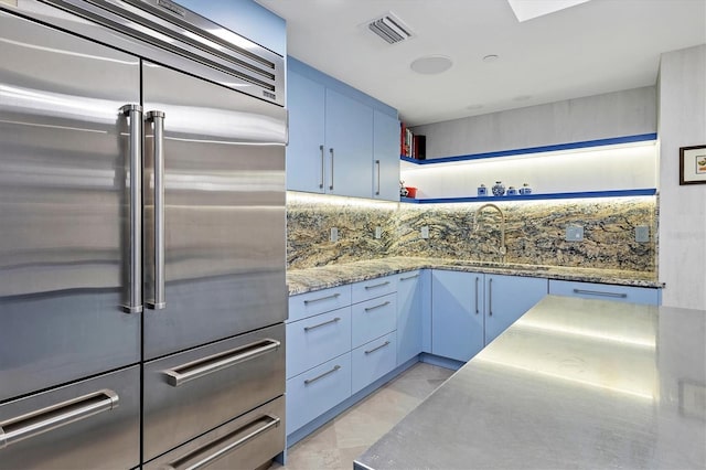 kitchen featuring stone countertops, blue cabinets, sink, decorative backsplash, and stainless steel built in fridge