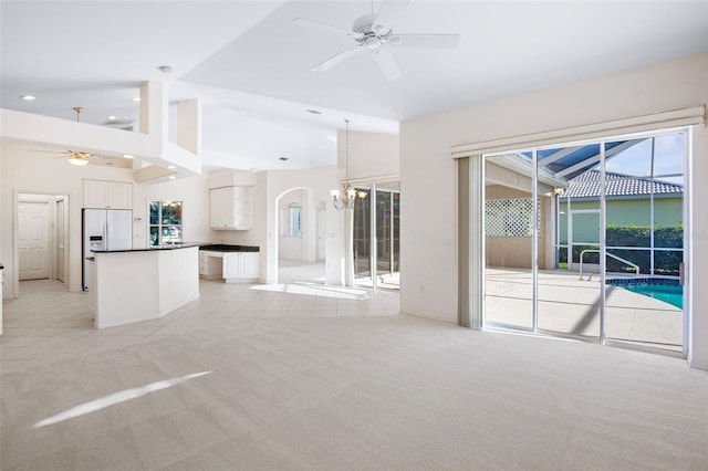 unfurnished living room featuring lofted ceiling, light colored carpet, and ceiling fan with notable chandelier