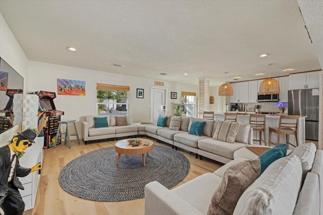 living room with ornate columns, a textured ceiling, and light wood-type flooring