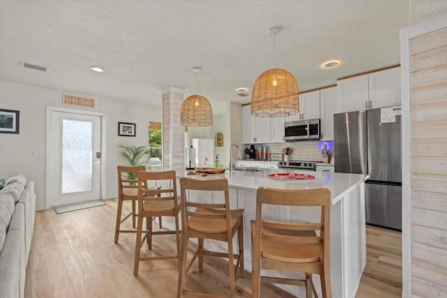 kitchen with a breakfast bar, white cabinetry, appliances with stainless steel finishes, pendant lighting, and a kitchen island with sink