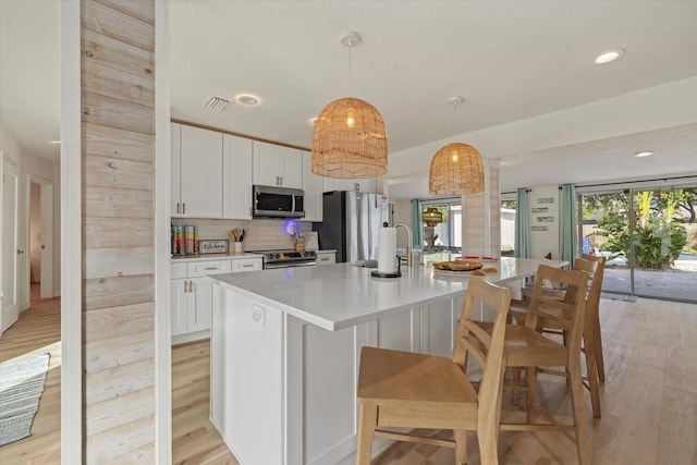 kitchen with appliances with stainless steel finishes, an island with sink, hanging light fixtures, and white cabinets