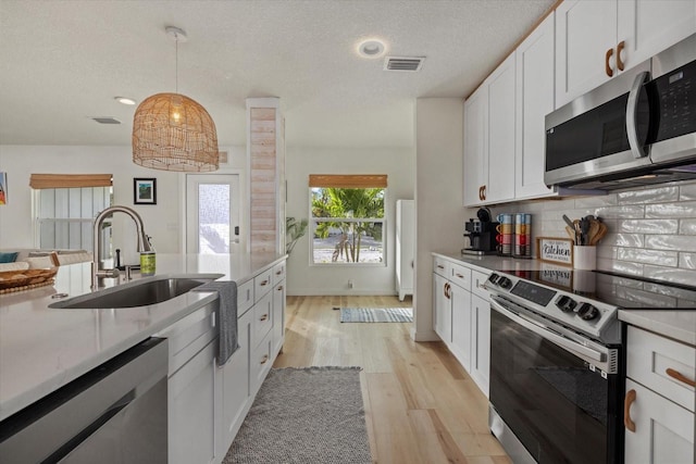 kitchen with appliances with stainless steel finishes, pendant lighting, white cabinetry, sink, and light wood-type flooring