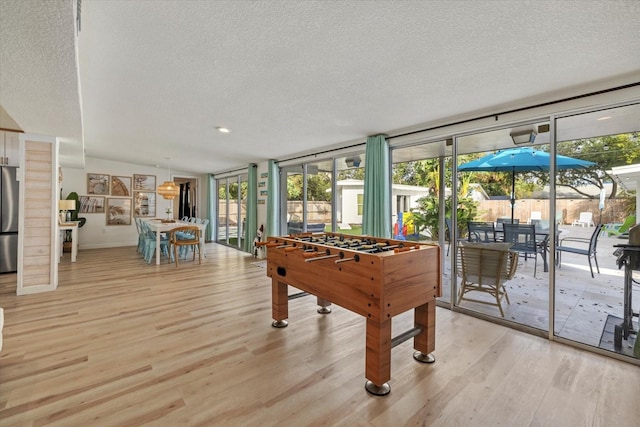 game room featuring a healthy amount of sunlight, a textured ceiling, and light wood-type flooring