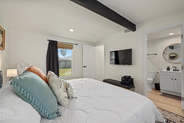 bedroom with connected bathroom, vaulted ceiling with beams, light hardwood / wood-style floors, and sink