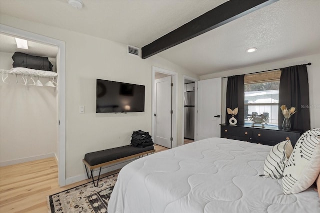 bedroom featuring a walk in closet, lofted ceiling with beams, a textured ceiling, stainless steel fridge, and hardwood / wood-style floors