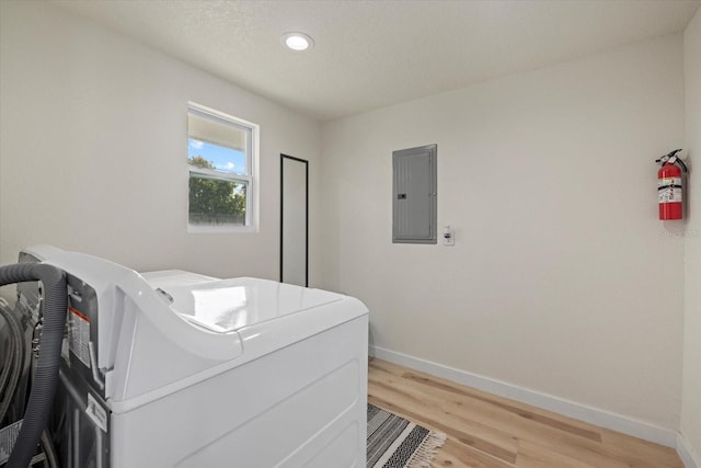 washroom featuring a textured ceiling, electric panel, washer and clothes dryer, and light hardwood / wood-style floors