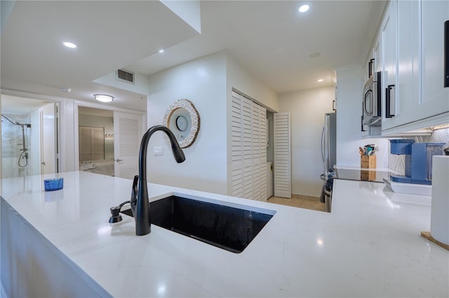 kitchen featuring white cabinetry, sink, light stone counters, and appliances with stainless steel finishes