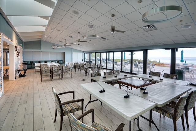 dining room with light wood-type flooring, a drop ceiling, ceiling fan, a water view, and a high ceiling