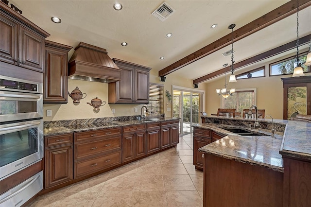 kitchen featuring hanging light fixtures, dark stone countertops, stovetop, dark brown cabinets, and custom range hood