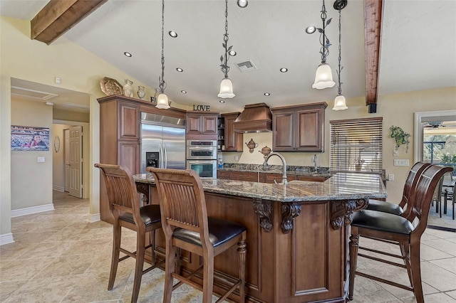 kitchen with a kitchen breakfast bar, dark stone counters, custom range hood, stainless steel appliances, and decorative light fixtures