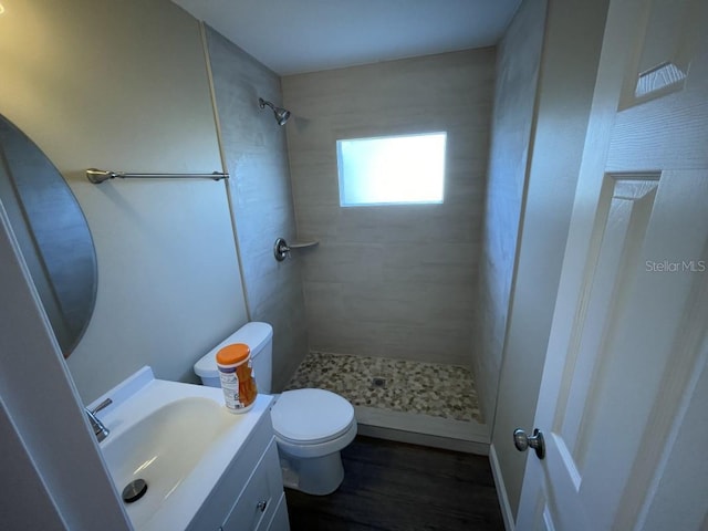 bathroom with tiled shower, hardwood / wood-style floors, vanity, and toilet