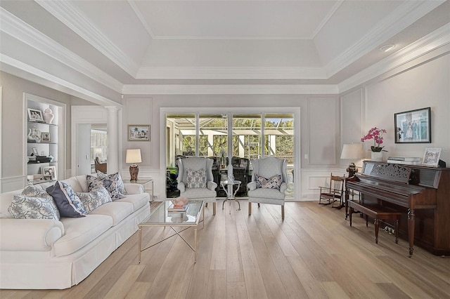 living room featuring decorative columns, a tray ceiling, ornamental molding, and light wood-type flooring