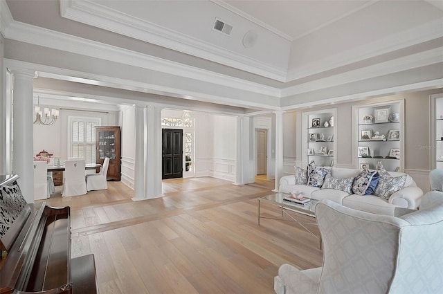 living room featuring crown molding, built in shelves, a chandelier, light wood-type flooring, and decorative columns