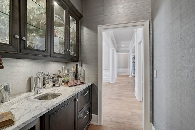 bar featuring light stone counters, sink, dark brown cabinets, and light hardwood / wood-style flooring