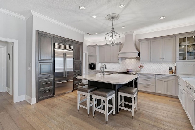 kitchen featuring appliances with stainless steel finishes, custom exhaust hood, a breakfast bar, sink, and hanging light fixtures