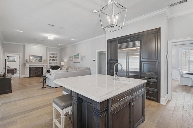 kitchen featuring sink, built in refrigerator, light stone countertops, an island with sink, and a breakfast bar area