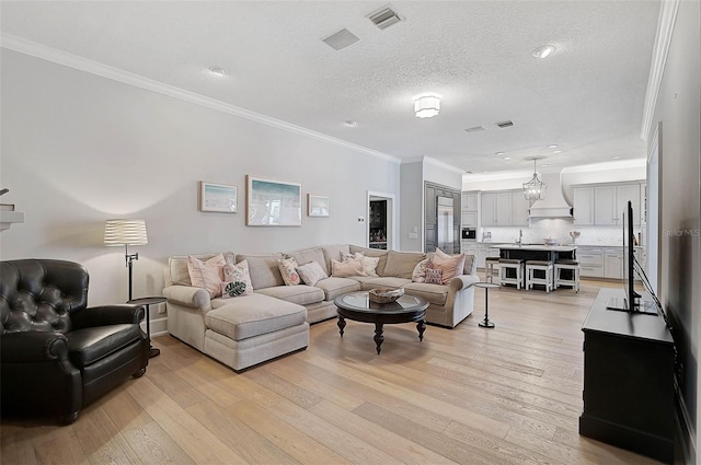 living room featuring light wood-type flooring, a textured ceiling, an inviting chandelier, and crown molding