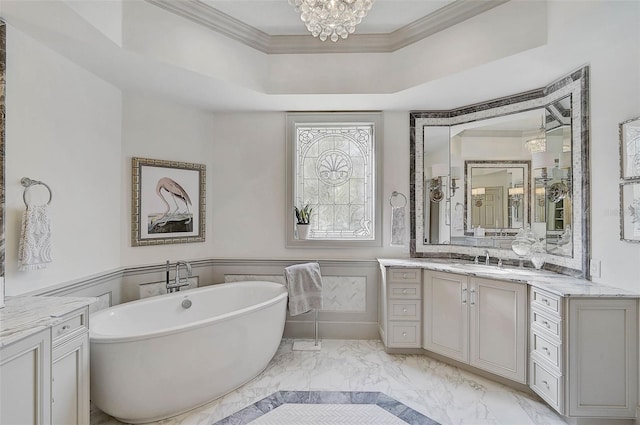 bathroom featuring vanity, an inviting chandelier, ornamental molding, a tub to relax in, and a tray ceiling