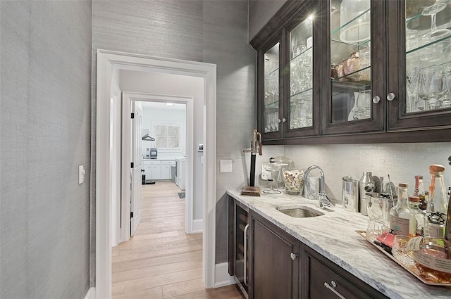 bar featuring dark brown cabinetry, light stone countertops, sink, wine cooler, and light wood-type flooring