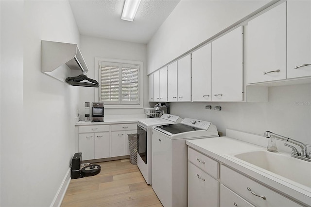 clothes washing area with sink, cabinets, a textured ceiling, washer and dryer, and light wood-type flooring