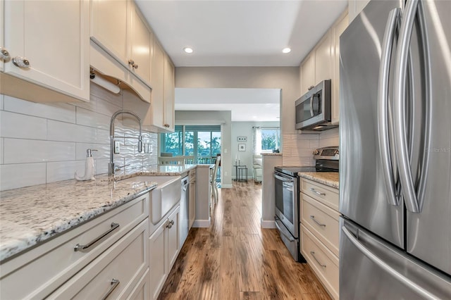 kitchen with decorative backsplash, light stone counters, stainless steel appliances, light hardwood / wood-style flooring, and white cabinetry