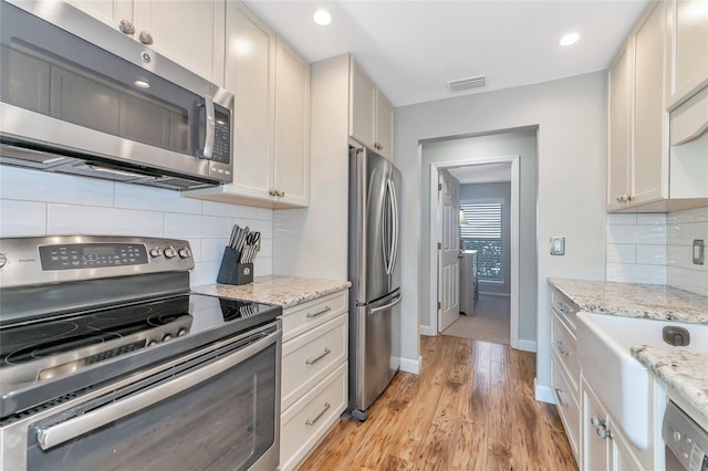 kitchen with decorative backsplash, light hardwood / wood-style flooring, light stone countertops, and appliances with stainless steel finishes