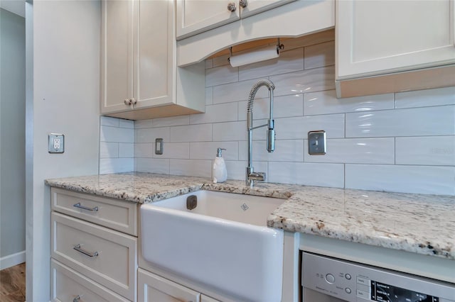 kitchen with light stone countertops, dishwasher, sink, backsplash, and hardwood / wood-style floors