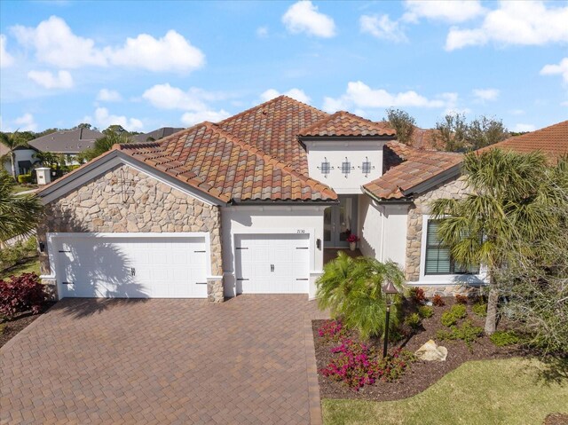 mediterranean / spanish-style house with stone siding, a tile roof, an attached garage, decorative driveway, and stucco siding