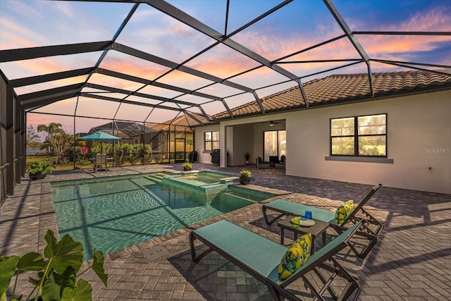 pool at dusk featuring ceiling fan, a patio area, a lanai, and a pool with connected hot tub