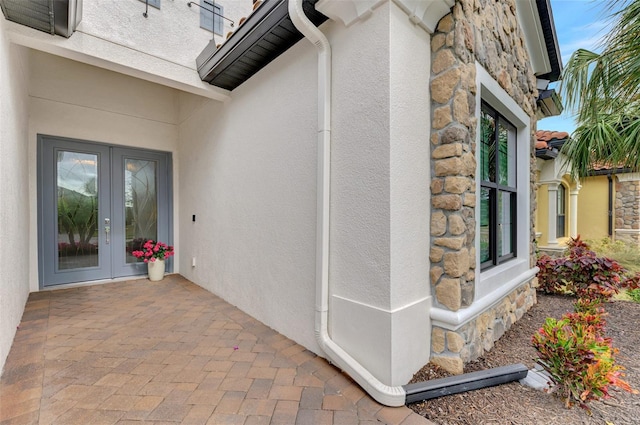 view of exterior entry with stucco siding, stone siding, and french doors