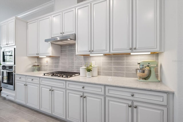 kitchen with appliances with stainless steel finishes, backsplash, white cabinetry, and under cabinet range hood