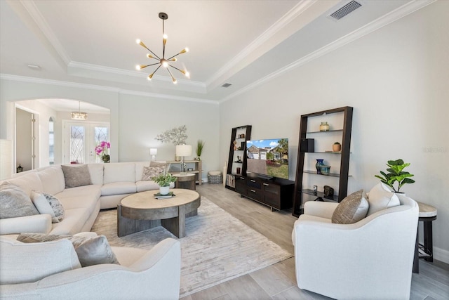 living area featuring light wood finished floors, visible vents, a raised ceiling, arched walkways, and an inviting chandelier