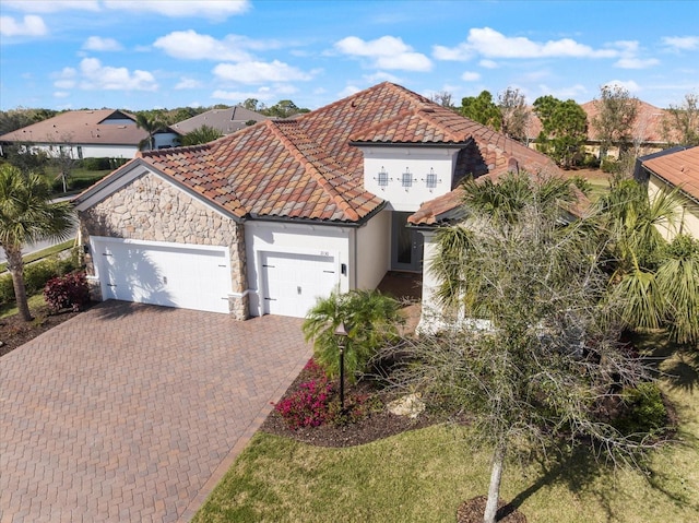 mediterranean / spanish home with a garage, stone siding, decorative driveway, and a tile roof