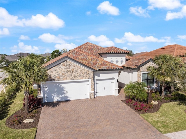 mediterranean / spanish house with an attached garage, a tile roof, stone siding, decorative driveway, and stucco siding