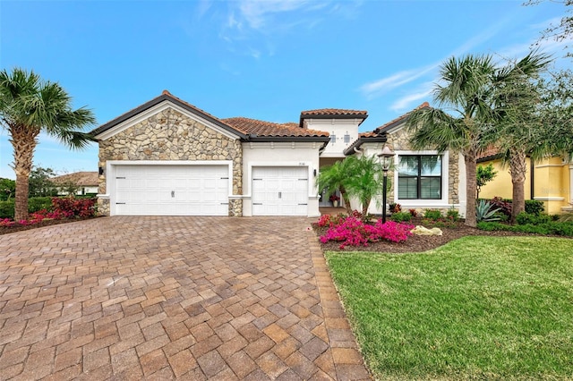 mediterranean / spanish-style house featuring a tile roof, stone siding, a garage, a front yard, and decorative driveway