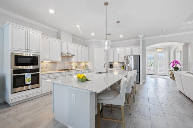 kitchen with arched walkways, stainless steel appliances, a sink, white cabinetry, and french doors