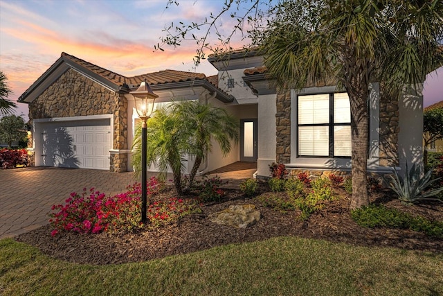 view of front of property featuring stone siding, decorative driveway, stucco siding, a tiled roof, and an attached garage