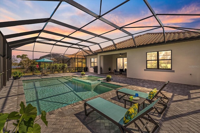 view of swimming pool featuring glass enclosure, ceiling fan, a pool with connected hot tub, and a patio area