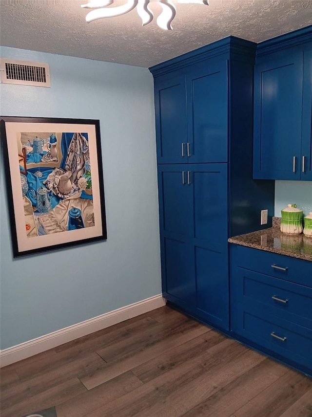 kitchen featuring a textured ceiling, dark hardwood / wood-style flooring, blue cabinets, and dark stone countertops