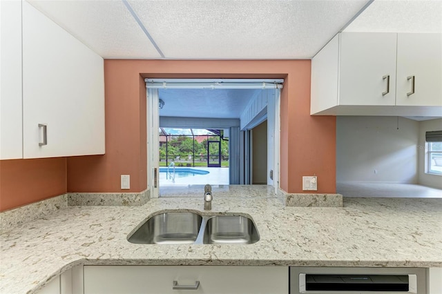 kitchen with light stone countertops, dishwashing machine, white cabinets, a textured ceiling, and a sink