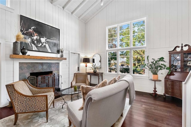 living room with beam ceiling, dark hardwood / wood-style flooring, high vaulted ceiling, wood walls, and a tiled fireplace