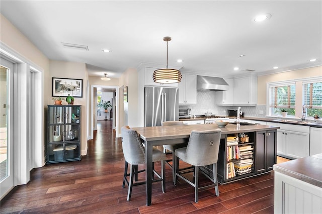 kitchen featuring dark wood-type flooring, pendant lighting, wall chimney range hood, and appliances with stainless steel finishes