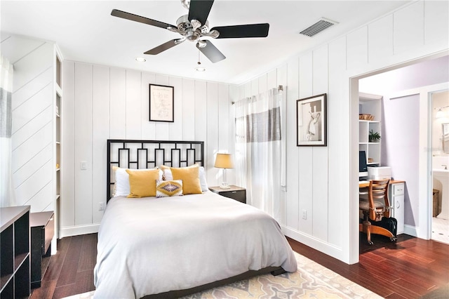 bedroom with ensuite bath, ceiling fan, dark hardwood / wood-style flooring, and wooden walls