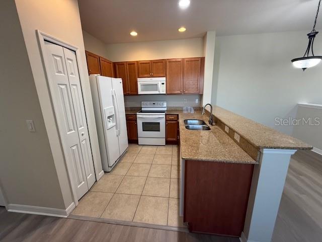 kitchen with kitchen peninsula, light wood-type flooring, white appliances, sink, and hanging light fixtures