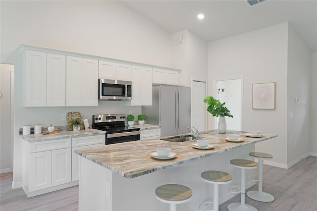 kitchen with appliances with stainless steel finishes, light stone counters, white cabinets, a high ceiling, and an island with sink