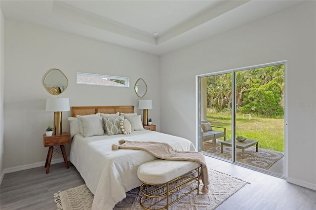 bedroom featuring hardwood / wood-style floors, access to outside, and a raised ceiling